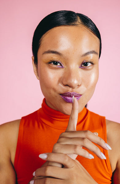Woman with bold lipstick doing a hush sign in a studio, looking at the camera