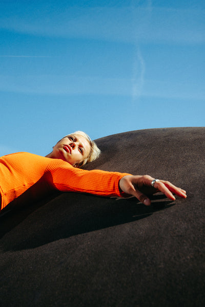 Fashionable woman in orange top relaxes on urban concrete surface