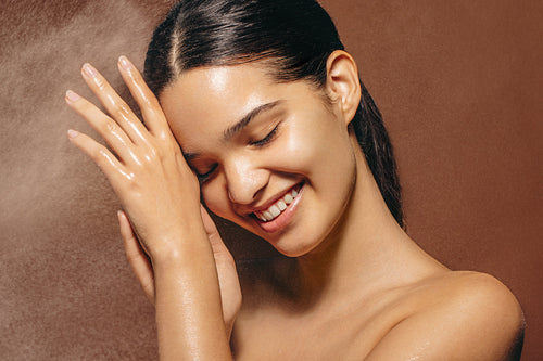 Refreshed and happy, woman stands under a shower with a smile