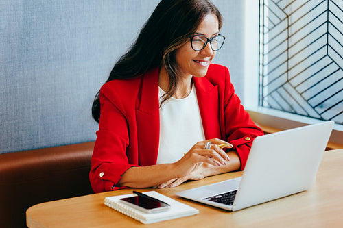 Professional woman in a red blazer working on a laptop computer