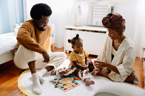 Parents playing with their toddler at home on bedroom floor