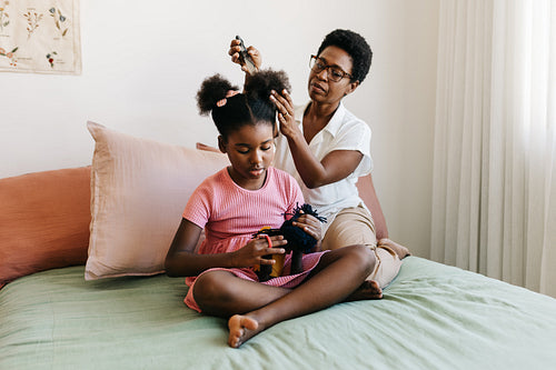 Mother doing her daughter's Afro hair in a bedroom, combing and styling it into hair buns