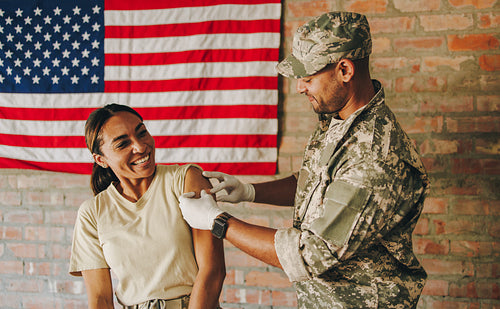 Young medic applying a band aid to a soldier's arm after vaccina
