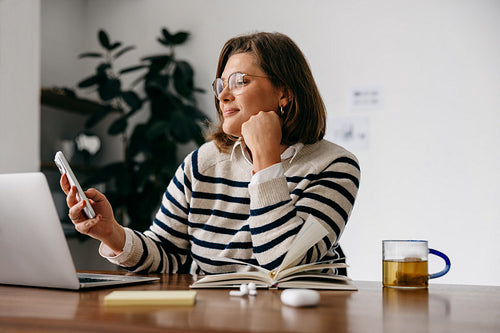 Multitasking between phone and laptop, the woman stays productive in a home office