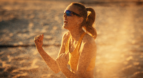 Happy female volleyball player celebrating victory on the beach at sunset