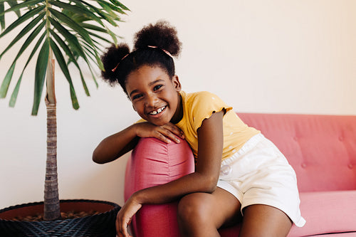 Cheerful afro-brazilian girl sitting on sofa at home, confidently smiling at camera