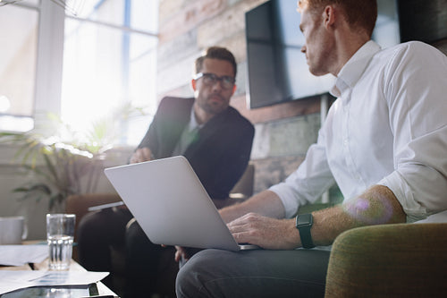 Businessman with laptop talking with colleague during meeting