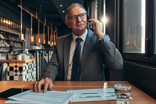 Confident senior businessman at coffee shop using phone