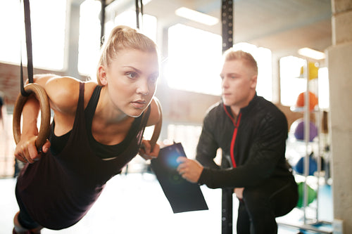 Woman with her personal trainer exercising on gymnastic rings