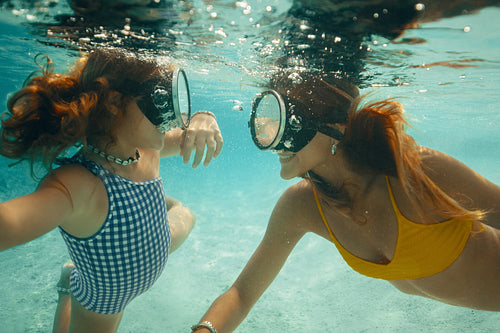 Underwater selfie of mother and daughter wearing masks enjoying summer pool fun