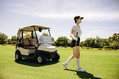 Female sportswoman in sports attire walking with a golf cart in the background