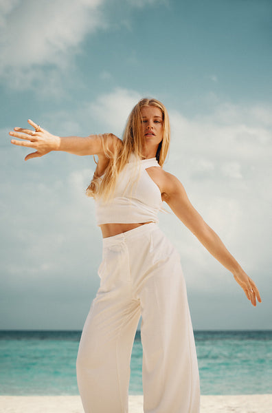 Young woman posing confidently on a beach in white attire beneath blue skies