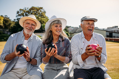 Senior people sitting together on a bench in a park holding boules