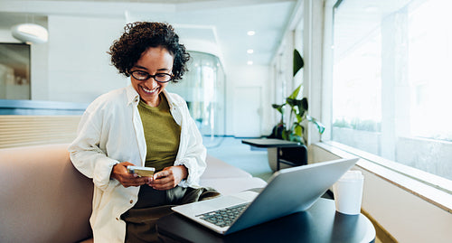 Woman smiling as she uses phone with laptop nearby