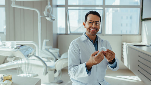Smiling dentist holding tooth model in dental clinic portrait