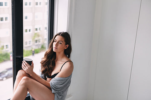 Young lady relaxing on window sill with a cup of coffee