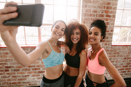 Happy young girls in sportswear taking selfie in gym
