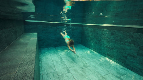 Young girl swims gracefully underwater in a serene private pool during a luxury island resort vacation