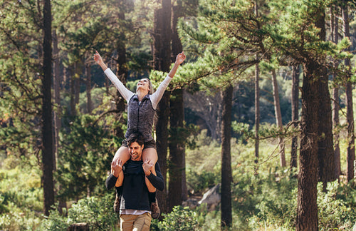 Man carrying his woman partner on his shoulders while trekking in forest