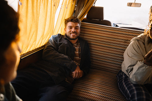 Relaxed friends share a smile during a sunny bus ride inside a cozy van