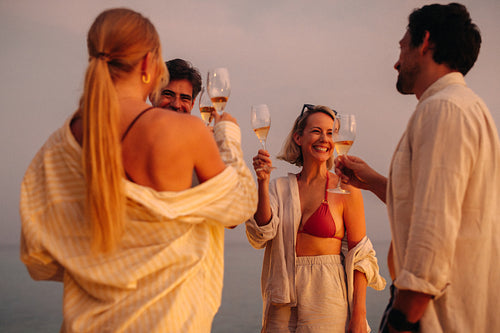 Group of friends toasting with champagne glasses at sunset on the beach
