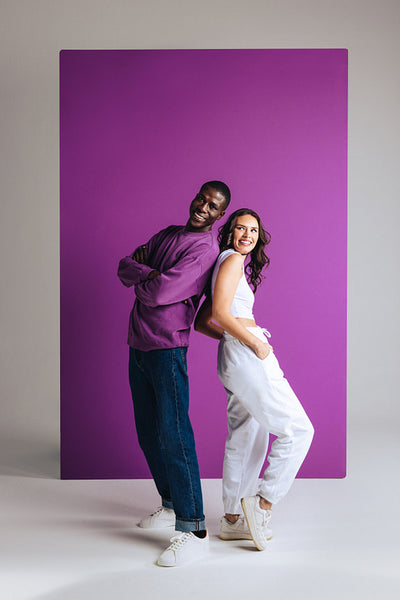 Two stylish young people wearing trendy clothing in a purple studio setting