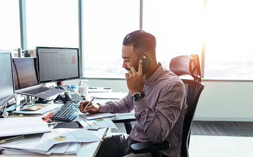 Entrepreneur discussing work over mobile phone sitting at his office desk.