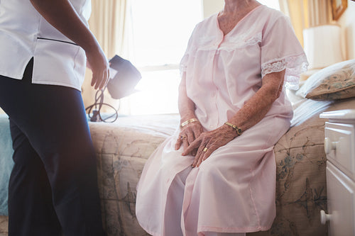 Home caregiver with senior woman sitting on bed