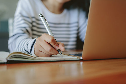 Student taking notes with laptop on table