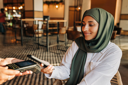 Muslim woman paying using a smartphone in a cafe
