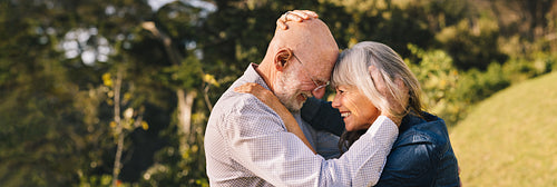 Elderly couple touching their heads together in a park