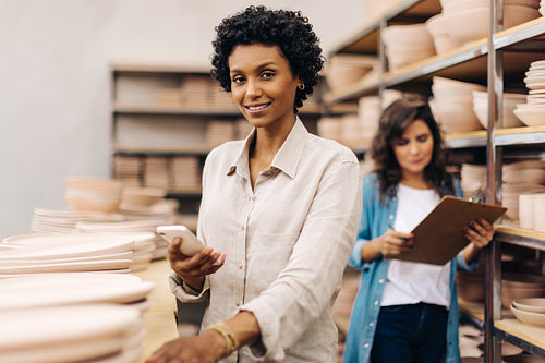Happy young ceramist using a smartphone in her shop