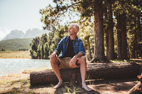 Senior man sitting on log and looking at the lake