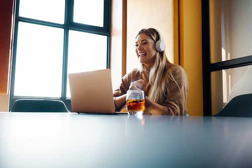 Young woman in headphones working on a project using a laptop in creative office