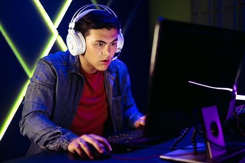 Young man focusing on the pc screen as he plays a video game online