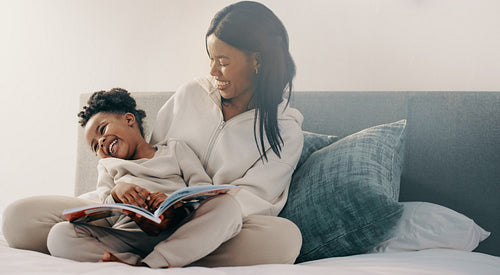 Preschool age girl laughs happily while sitting with her mom reading a story book
