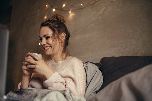 Cheerful woman drinking coffee in bedroom