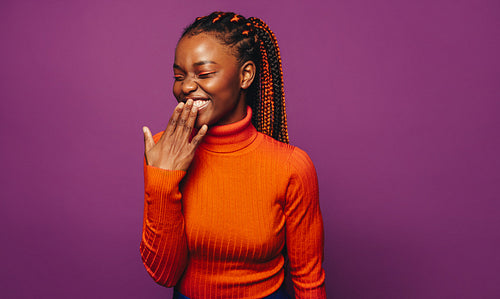 Happy and stylish young woman with vibrant two tone braids standing on colourful purple background