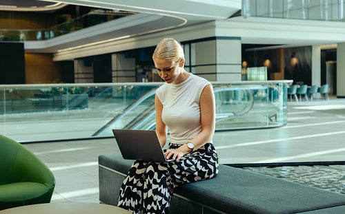 Woman working on laptop in modern office lobby setting