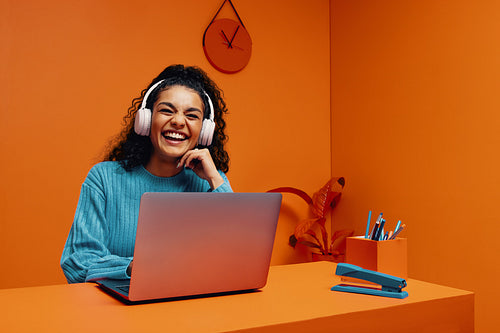 Joyful young woman listening to music and laughing while working on laptop