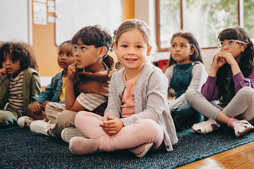 Adorable little child looking at the camera while sitting in class with other kids