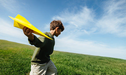 Boy launches yellow paper airplane in open field