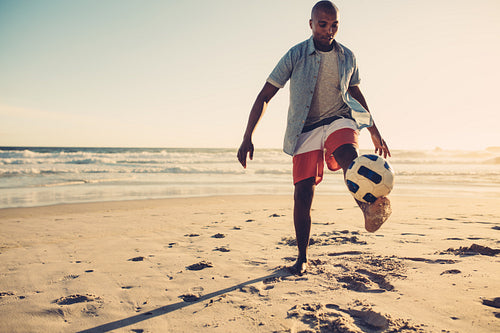 African man playing with soccer ball at beach