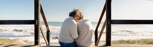Panoramic view of a senior woman sitting with her husband at the beach