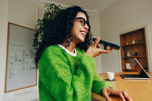 Woman talking on smartphone at office desk with laptop during work call