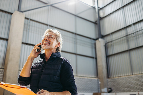 Happy senior man taking a phone call in a warehouse