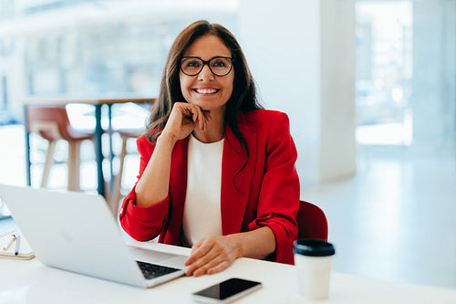 Smiling woman in red blazer working on laptop at bright office desk