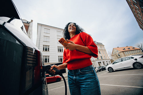 Woman uses smartphone app to charge electric car at urban station