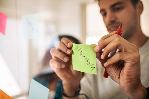 Businessman pasting sticky notes on glass wall in office