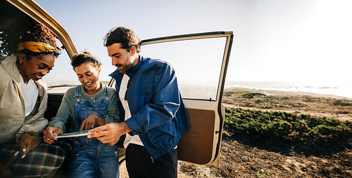 Friends explore a map by a car at the coastal overlook
